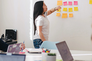 Business woman collecting and visualizing ideas using colorful sticky notes on a wall in a conference.