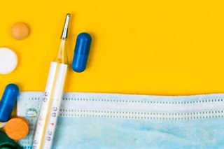 Collection of a blue mask, thermometer, and pills on a yellow background.